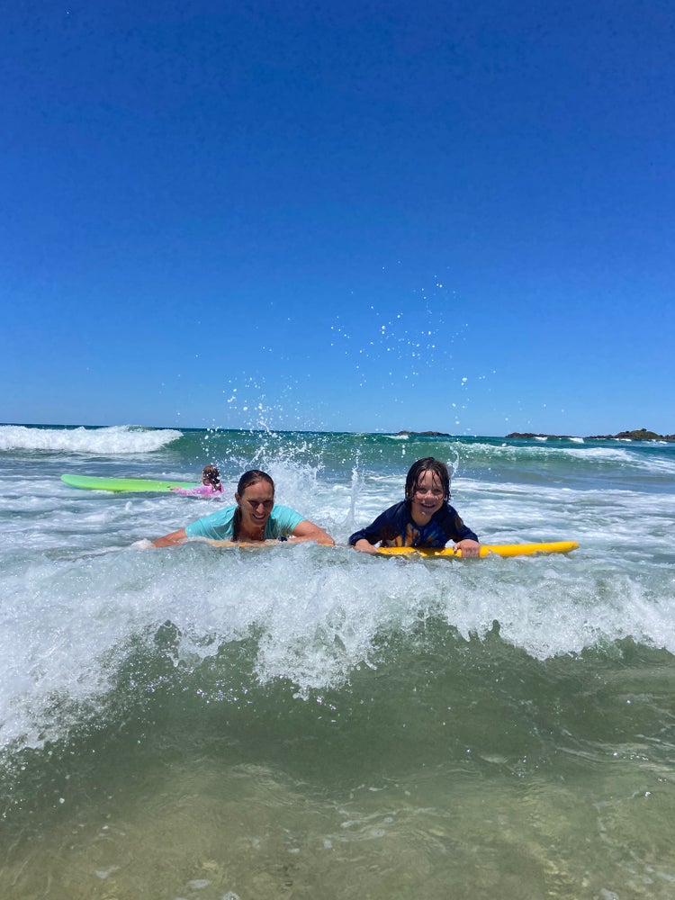 A student and teacher paddling sideways on a surfboard during our Ocean Safety Awareness Day at Sawtell Beach