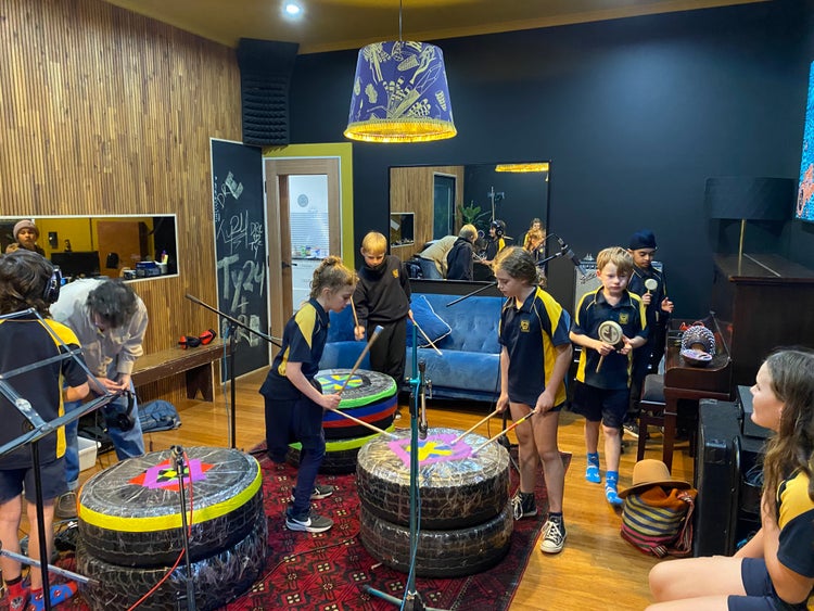 Students playing drums made from recycled materials at a recording studio whilst recording a song they created as part of the Oz-Green learnong on reducing waste.