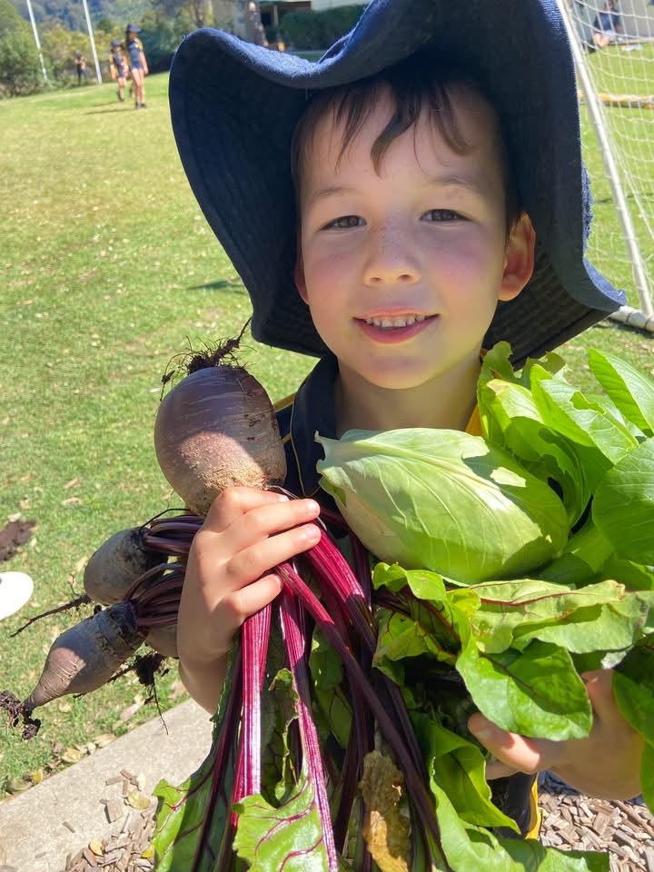 A K-2 student with his armsful of fresh produce from our garden for Kids in the Kitchen